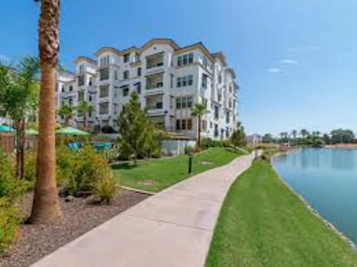 An exterior shot of the modern apartment building overlooking a manicured lawn, a palm-lined pathway, and a vibrant pool area. Residents can be seen socializing and enjoying the scenic community spaces.