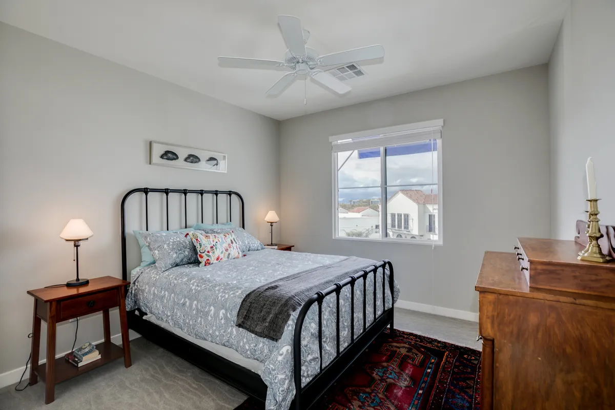 A well-appointed secondary bedroom with patterned bedding, a wooden dresser, and large windows letting in natural light, creating a peaceful, inviting space for guests or friends.
