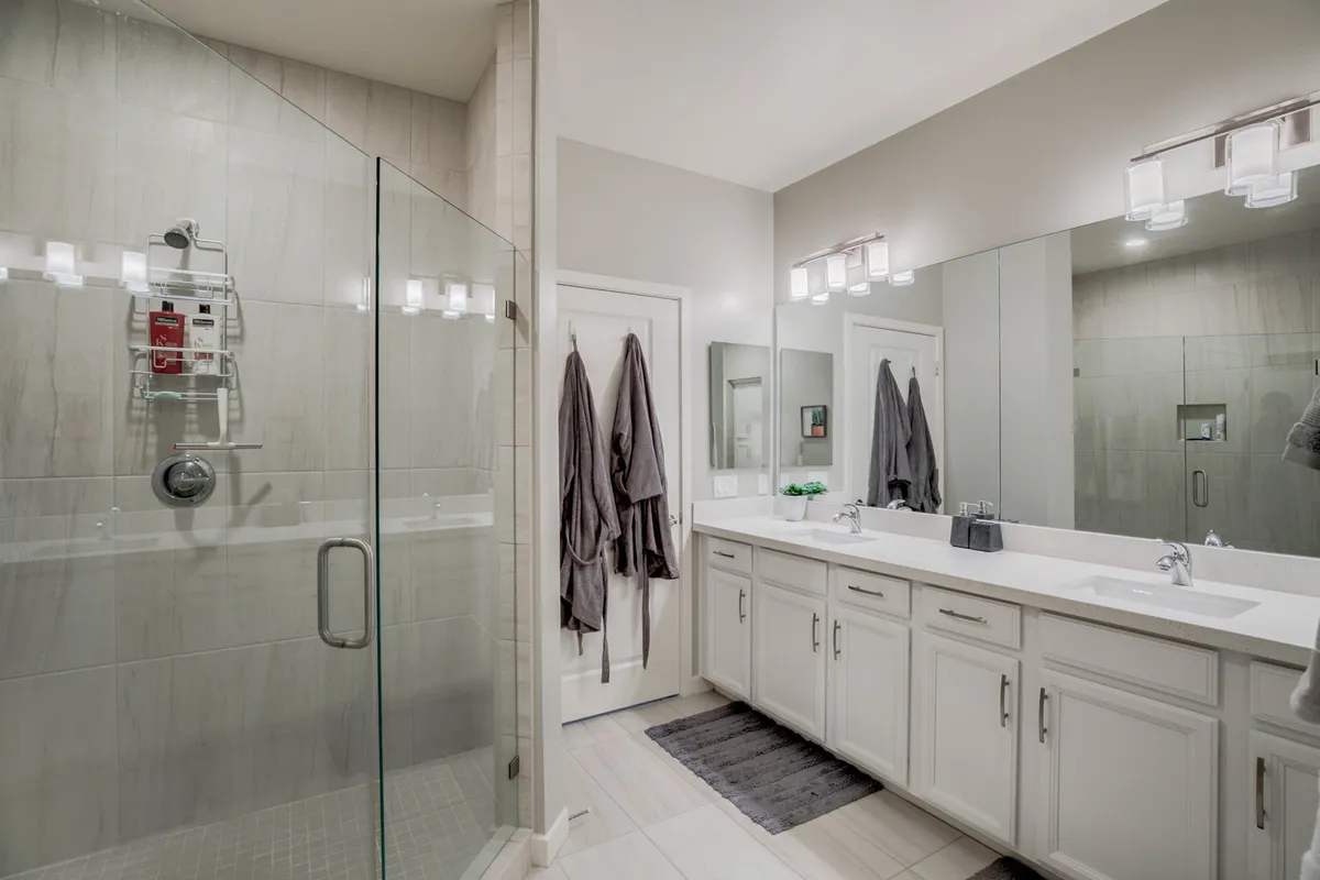 A modern, spa-inspired ensuite bathroom with a glass walk-in shower, double vanity with mirrors, and elegant lighting. The space exudes calm and luxury, ideal for unwinding after a long day.