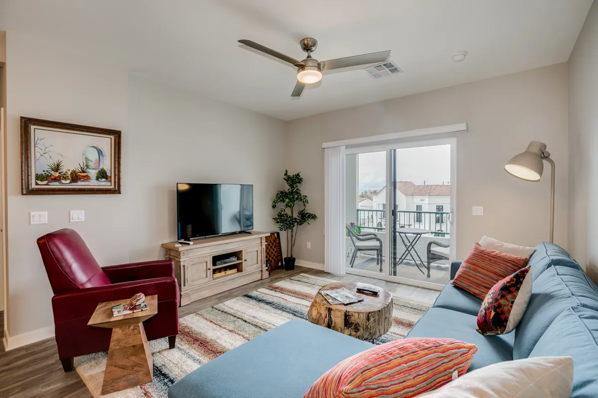 A colorful and cozy living area with a sofa, wooden coffee table, television, sliding glass door, and a potted plant. The sliding door hints at access to outdoor amenities, suggesting a seamless connection between indoor comfort and the resort's community spaces.