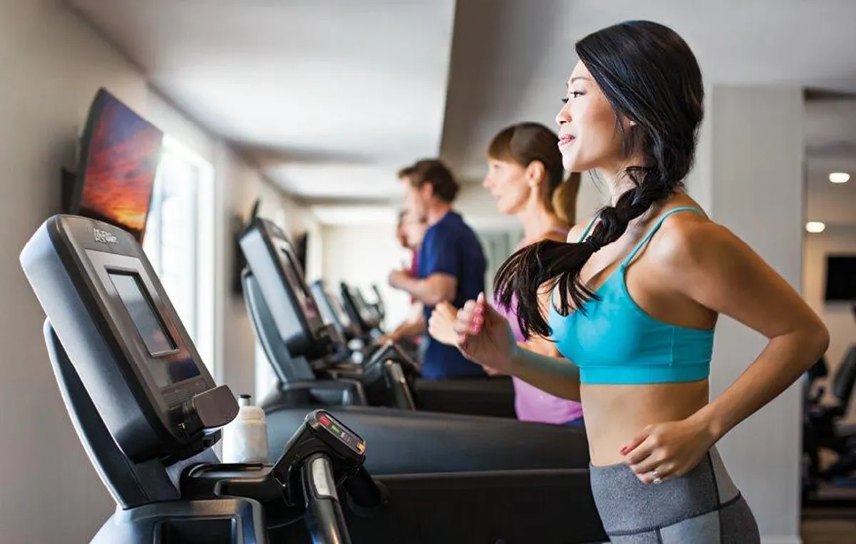 A vibrant fitness center scene with people working out on treadmills and a television screen providing entertainment. The space is bright, modern, and designed to motivate residents towards their wellness goals.