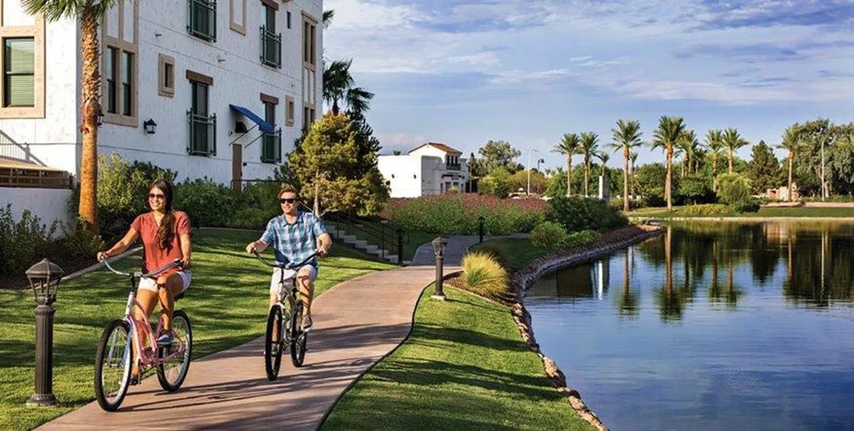 A lively waterfront path lined with palm trees, featuring bicyclists and walkers enjoying the natural scenery and reflecting water under a warm sky—a perfect representation of the active, walkable lifestyle near the property.